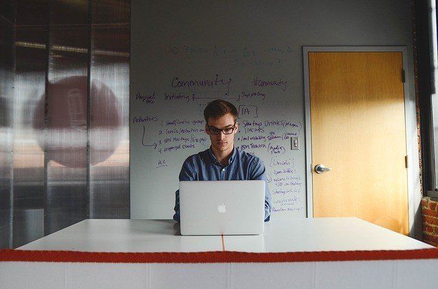 A man is sitting at a table using a laptop computer.